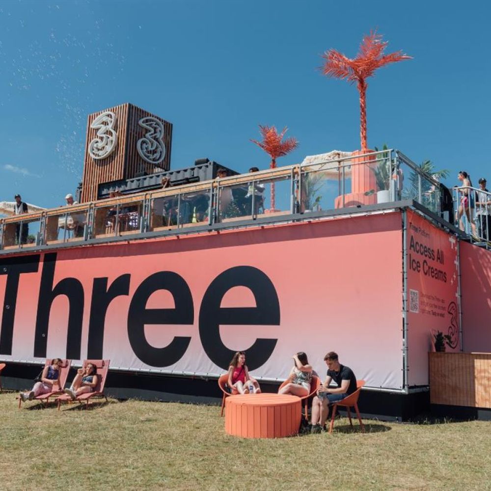 Three network stage with a lawn in front, people hanging out on chairs and deckchairs.